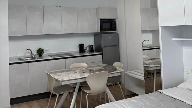 A modern, compact bedroom with a bed, a desk, and a kitchenette.