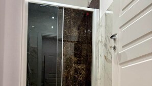 A modern bathroom with a glass shower enclosure, a white toilet, and a marble-tiled wall.