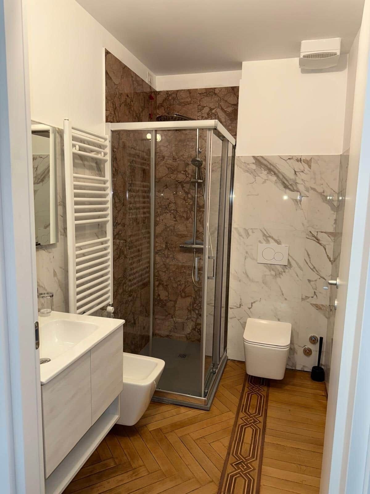 A modern bathroom with a glass-enclosed shower, a white toilet, and a vanity with a mirror.