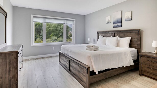 A bedroom with a large bed, a window with a view of greenery, and a wooden dresser. - Crosswinds Haven: 3BDR Backing onto Blue Mountain (The Blue Mountains)