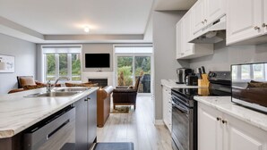 A modern kitchen with a central island, built-in appliances, and a large window providing a view of the outdoors. - Crosswinds Haven: 3BDR Backing onto Blue Mountain (The Blue Mountains)