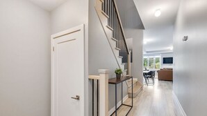 A modern interior with a staircase, a console table with a plant, and a view into a living area with a sofa and TV. - Crosswinds Haven: 3BDR Backing onto Blue Mountain (The Blue Mountains)