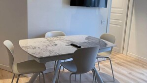 Un espace repas moderne avec une table en marbre, des chaises blanches et un téléviseur à écran plat fixé au mur.