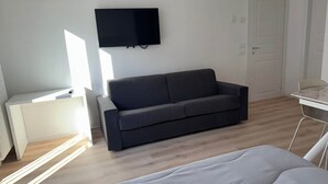 A modern, minimalistic room with a grey sofa, a flat-screen TV mounted on the wall, and a small desk with a chair. - Penthouse Apartment in Sforza Castle (Milan)