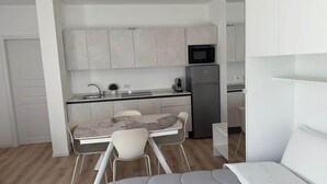 A compact kitchen with a built-in microwave, a refrigerator, and a small sink. There is a dining area with a marble table and four chairs. - Penthouse Apartment in Sforza Castle (Milan)