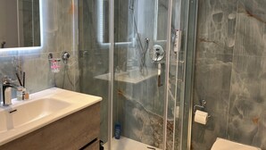 Ein modernes Badezimmer mit einer Duschkabine aus Glas, einem Waschbecken mit Spiegel und einer Toilette.