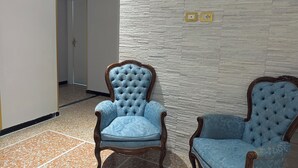 Ein Zimmer mit zwei gepolsterten Sesseln auf Holzgestell, einer strukturierten Wand und einem gefliesten Boden.