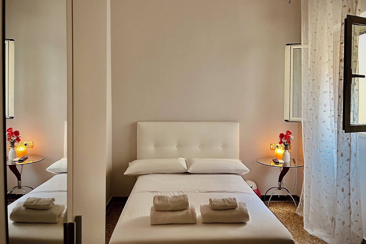 A hotel room with a bed, two bedside tables, a mirror, and a window with curtains.