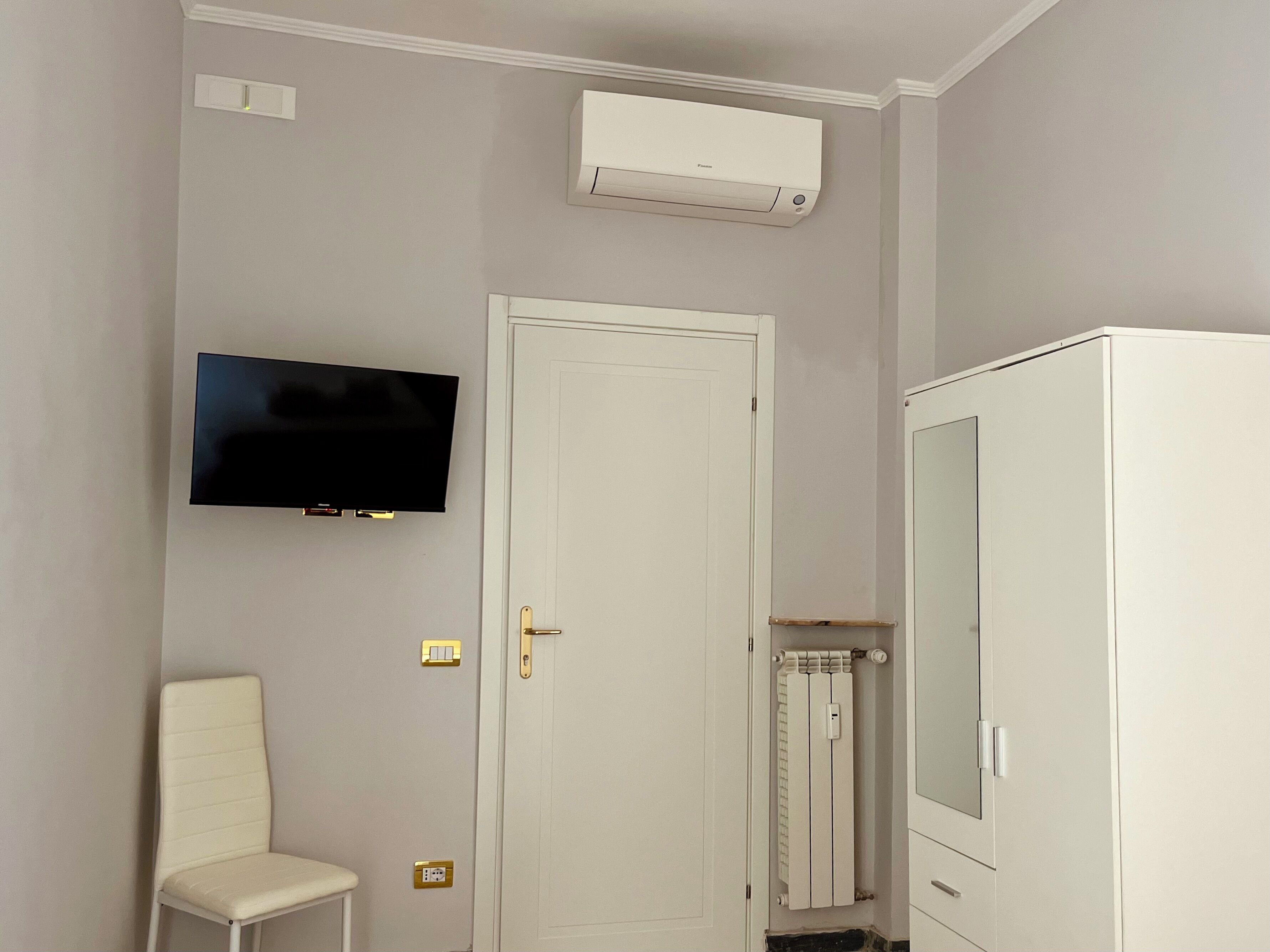 A room with a white wardrobe, a television mounted on the wall, a door, and a radiator.