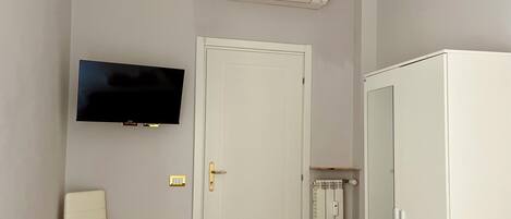 A room with a white wardrobe, a television mounted on the wall, a door, and a radiator.