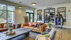 A spacious lobby with a leather sofa, a coffee table, and a seating area with a grey armchair. A boutique with clothing racks is visible in the background. - Golfside Tremblant Retreat | Private Hot Tub (Mont-Tremblant)