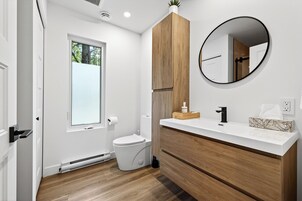 Un baño moderno con inodoro, lavamanos con espejo y muebles de madera.