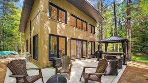 Une maison moderne à deux étages dotée d’un patio aménagé avec des fauteuils Adirondack, un foyer extérieur et un belvédère.