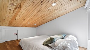 Une chambre avec un plafond en pente, un lit avec une literie blanche et un plancher en bois.