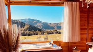 A wooden cabin with a hot tub, a large window with a mountain view, and a cozy seating area.