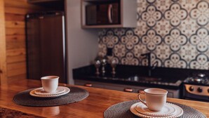 A kitchen with two cups on coasters, a microwave, and a patterned backsplash.