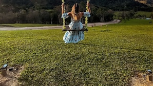 A woman on a swing in a grassy field with a hilly landscape in the background.
