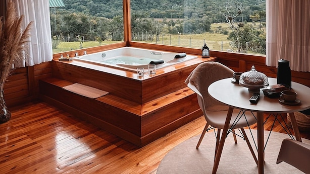 A wooden cabin with a hot tub, a dining area, and a view of a mountainous landscape.