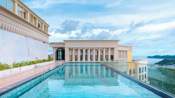 Una piscina infinita en la azotea con vistas despejadas al océano y un edificio clásico al fondo.