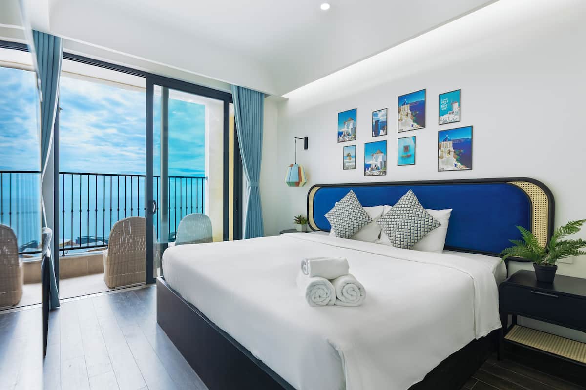 A hotel room with a large bed, a balcony with wicker chairs, and a view of the sea.