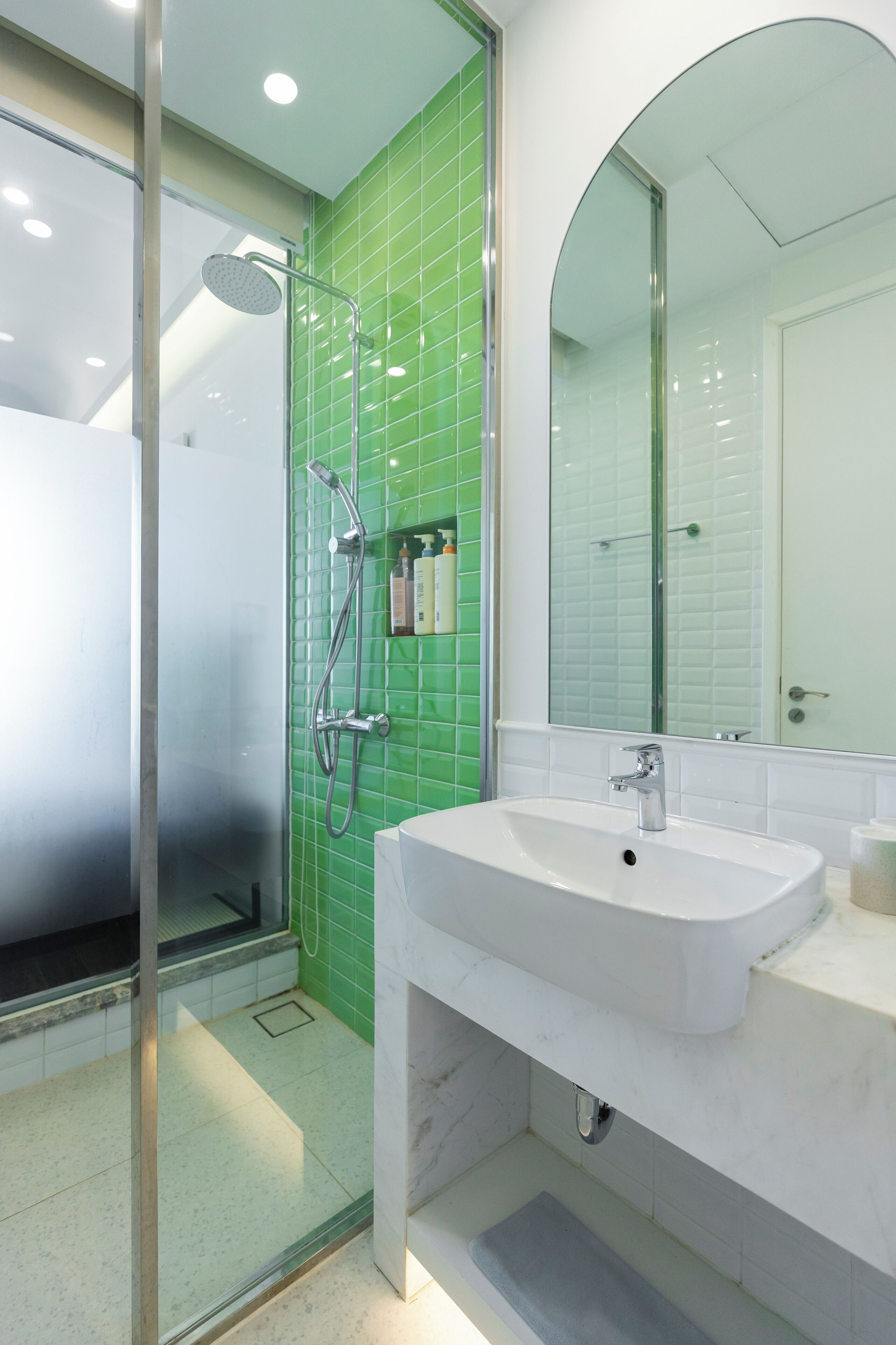 Un baño moderno con ducha de vidrio, lavamanos blanco y paredes con azulejos verdes.
