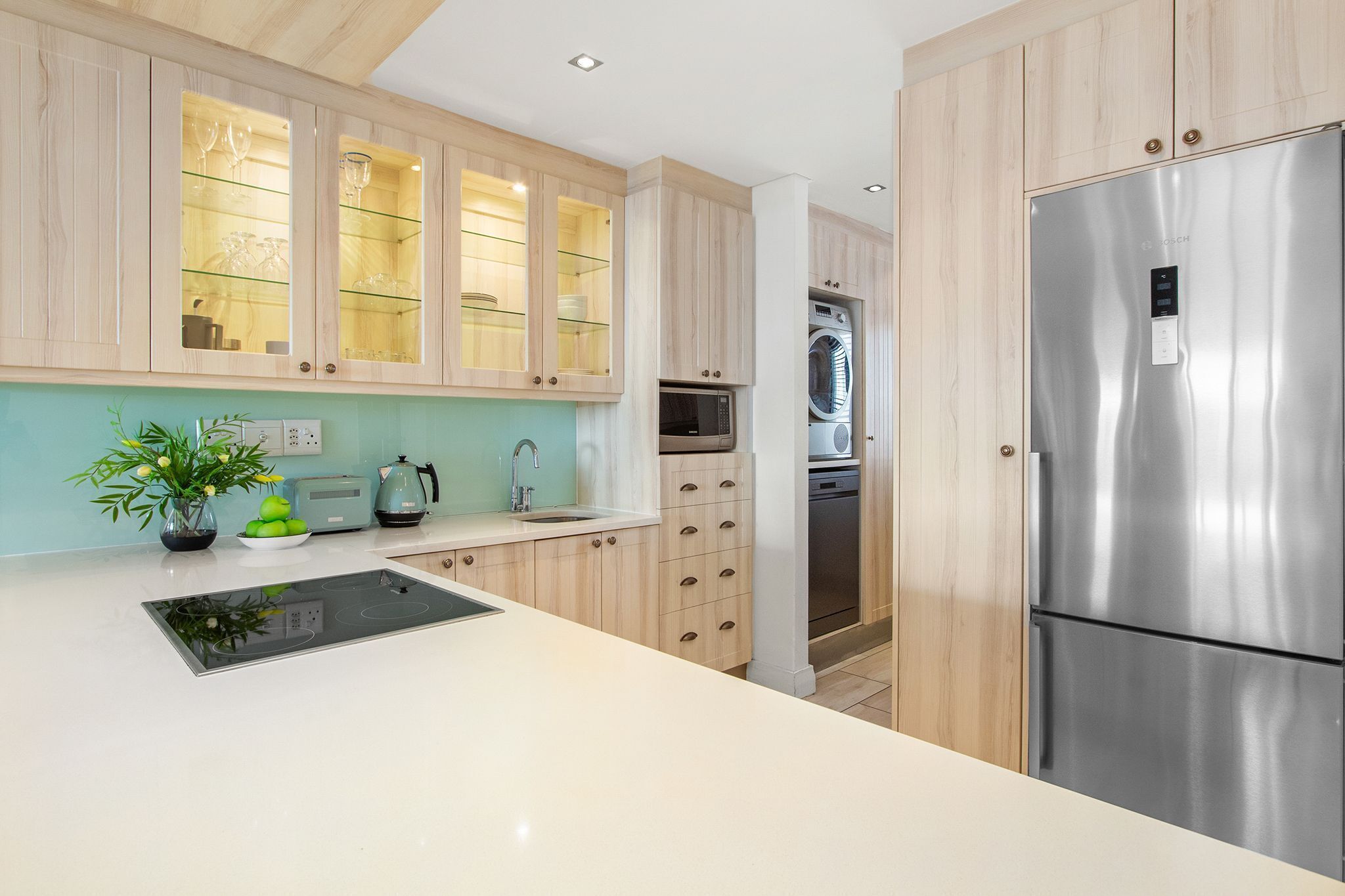 A modern kitchen with wooden cabinets, a stainless steel refrigerator, a microwave, and a sink.