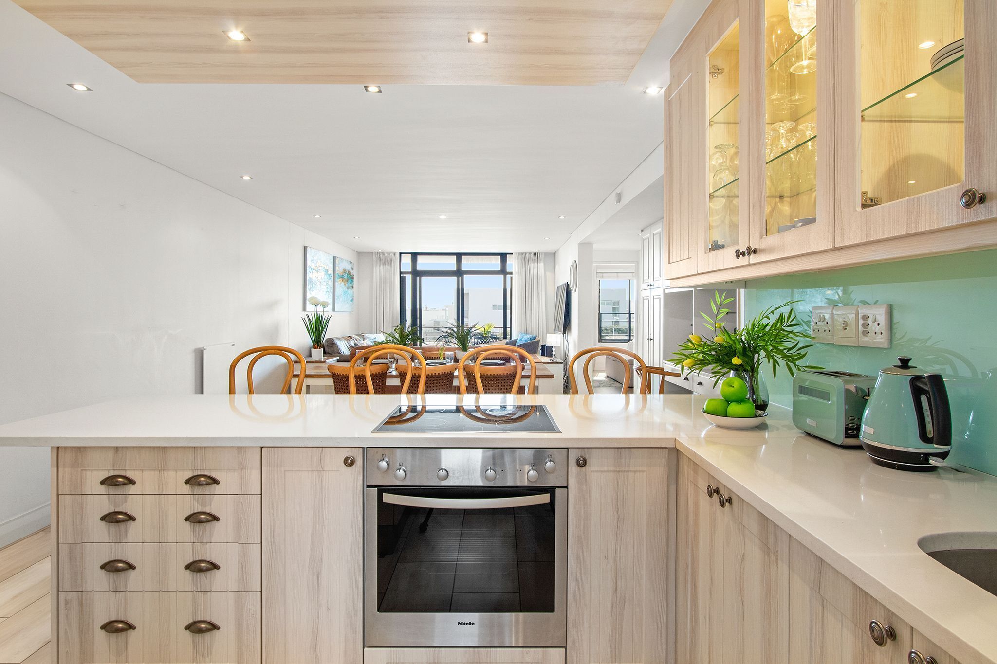 A modern kitchen with a central island, built-in oven, and a dining area with chairs.
