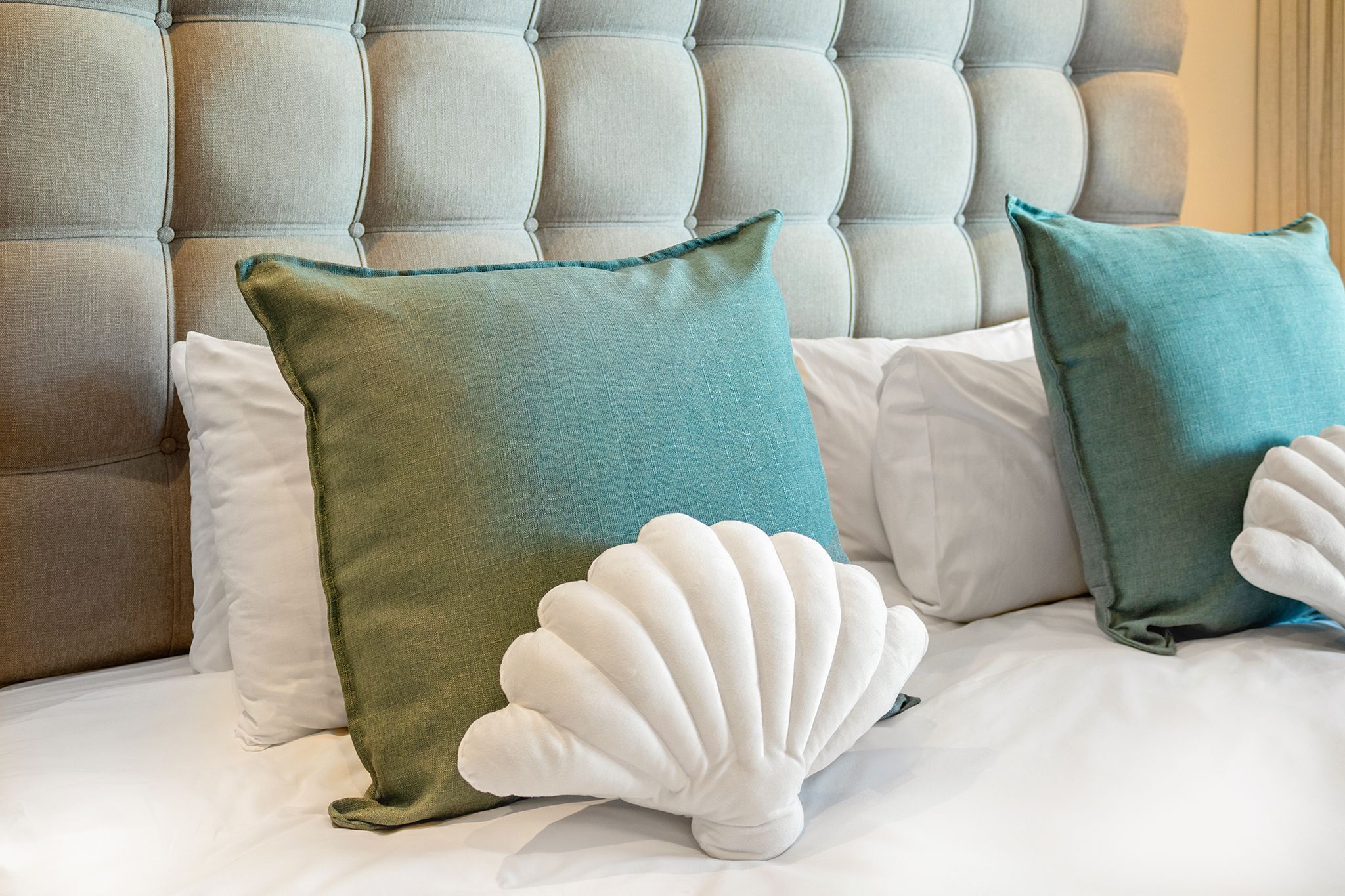 A bed with a tufted headboard, white and teal pillows, and a white seashell-shaped pillow.