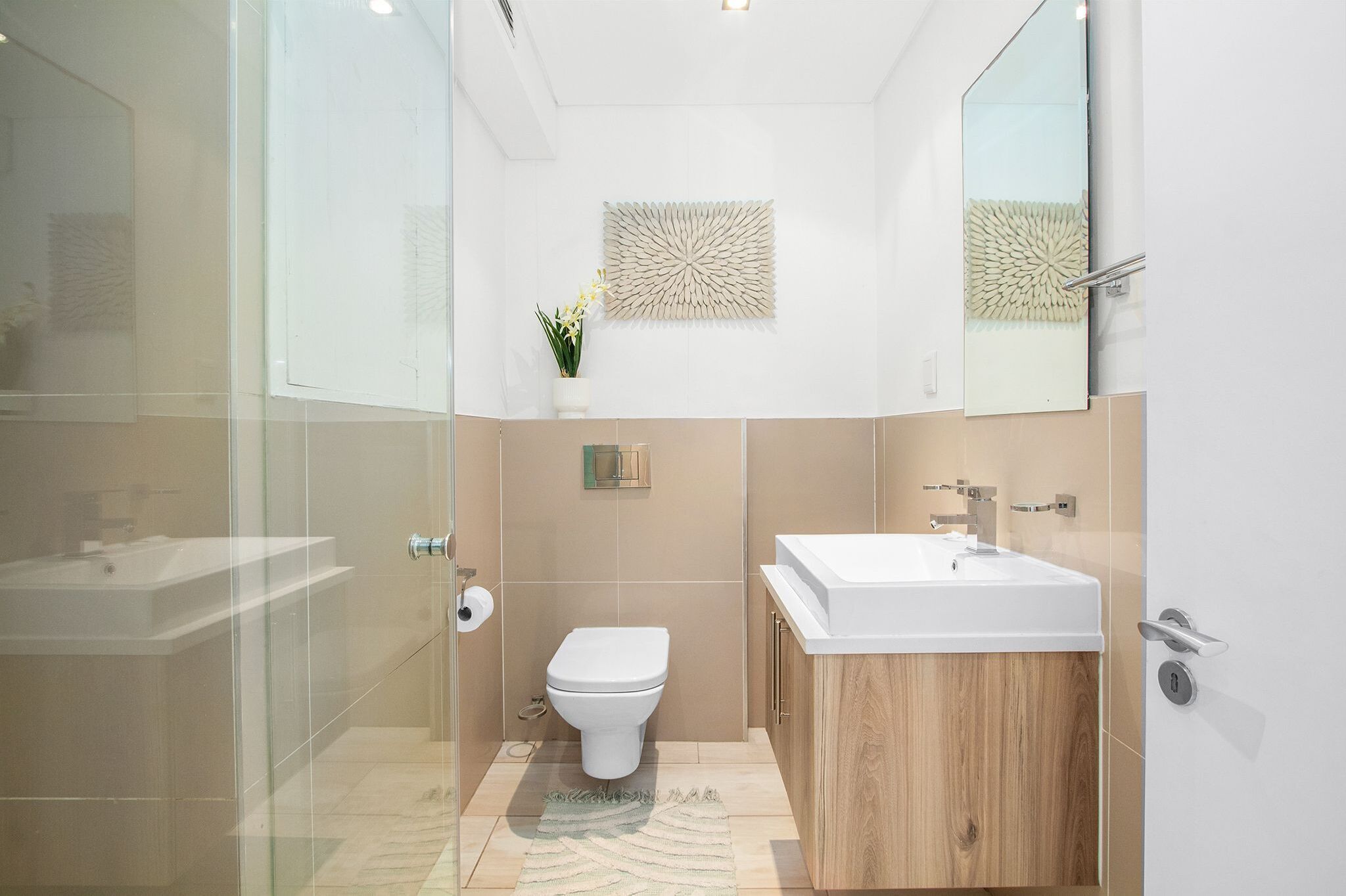 A modern bathroom with a glass shower enclosure, a wooden vanity, and a toilet.