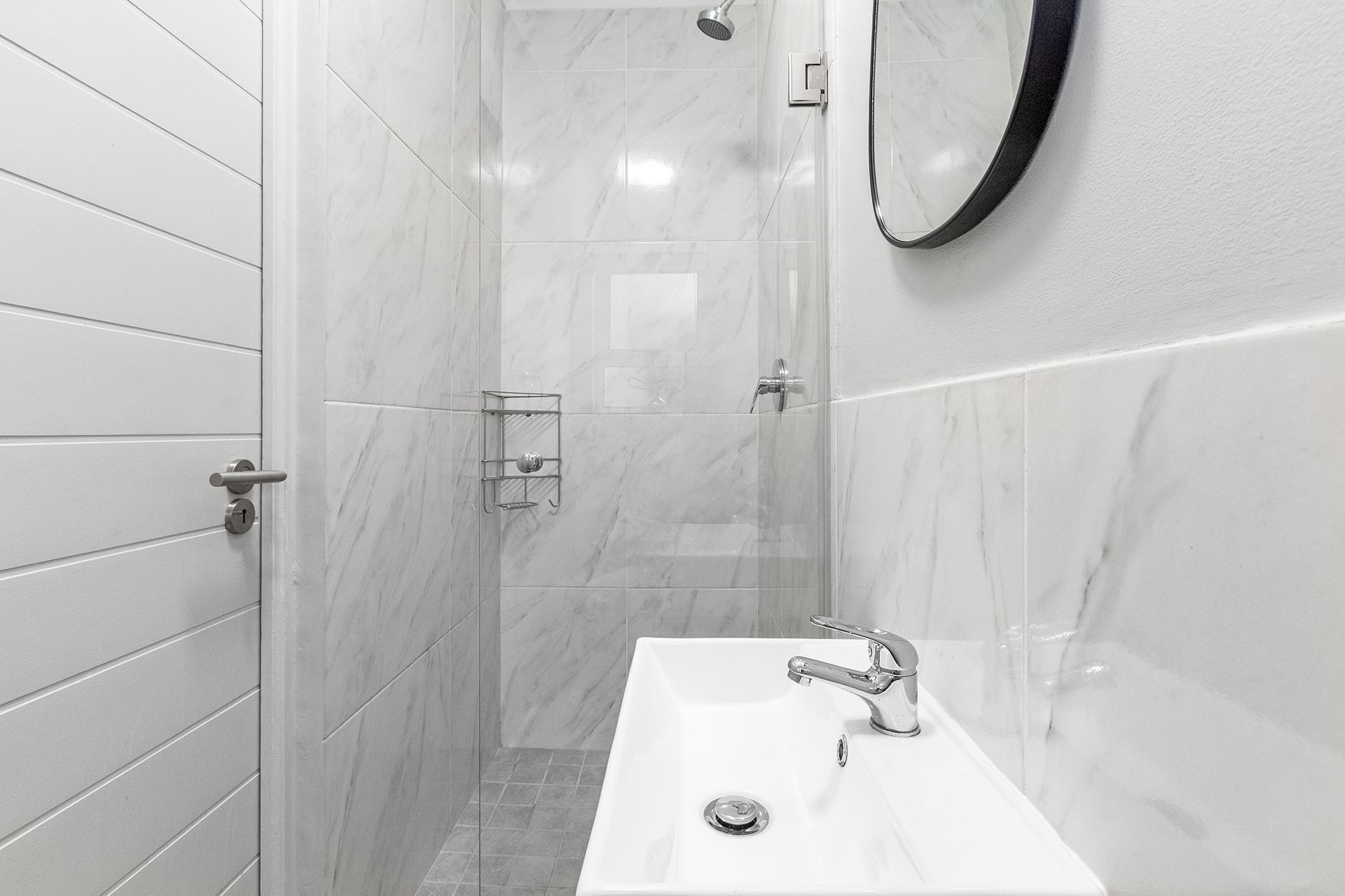 Un baño moderno con un lavamanos blanco, ducha y espejo.