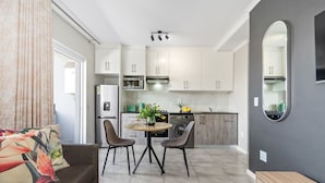 A modern kitchen with white cabinets, a dining area with two chairs, a round table, and a sofa with a floral cushion.