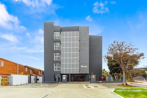 Un edificio moderno con un letrero con su nombre, fachada con diseño y entrada protegida por una reja.