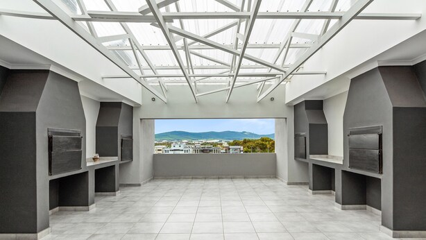A spacious room with a high ceiling and skylight, featuring a large window with a view of distant buildings and mountains.