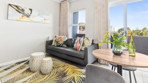 A modern living room with a grey sofa, patterned ottomans, a round wooden table, and a large window with curtains.