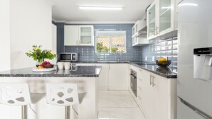 A modern kitchen with white cabinets, a granite countertop, a water dispenser, and a window with a view of greenery. - Big Bay Beach Club 137 (Blouberg)