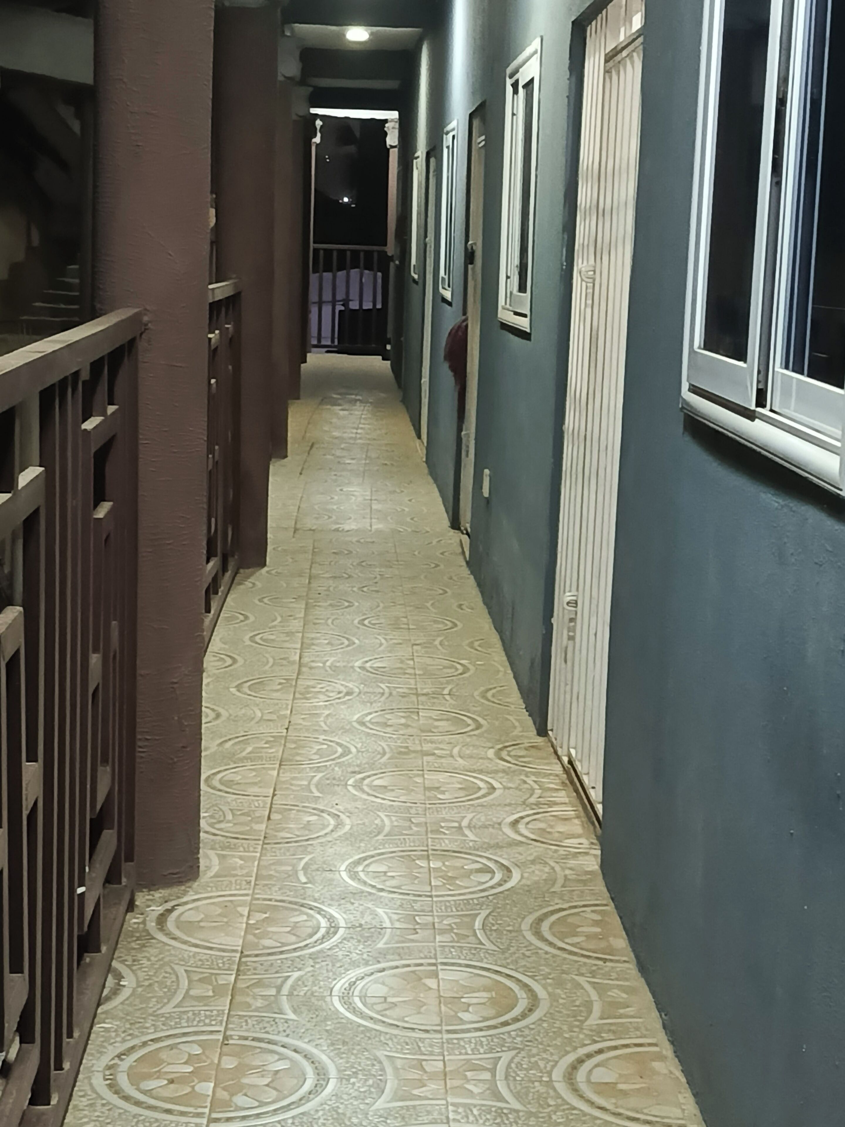 Un couloir avec des carreaux de sol à motifs, une rambarde en métal d’un côté et une porte de l’autre.