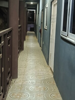 A hallway with patterned floor tiles, a metal railing on one side, and a door on the other.