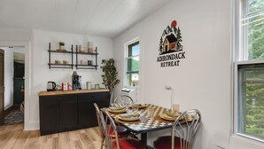 A dining area with a checkered table, red chairs, and a kitchen in the background. - Condo with Backyard Oasis on Ausable River (Wilmington)