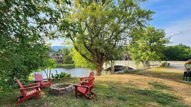A lakeside outdoor seating area with Adirondack chairs and a fire pit. - Condo with Backyard Oasis on Ausable River (Wilmington)