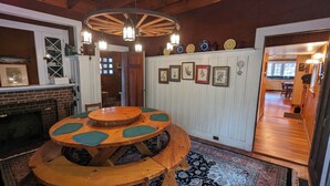 Un comedor con una mesa y sillas de madera, chimenea de ladrillo y un pasillo con cuadros.