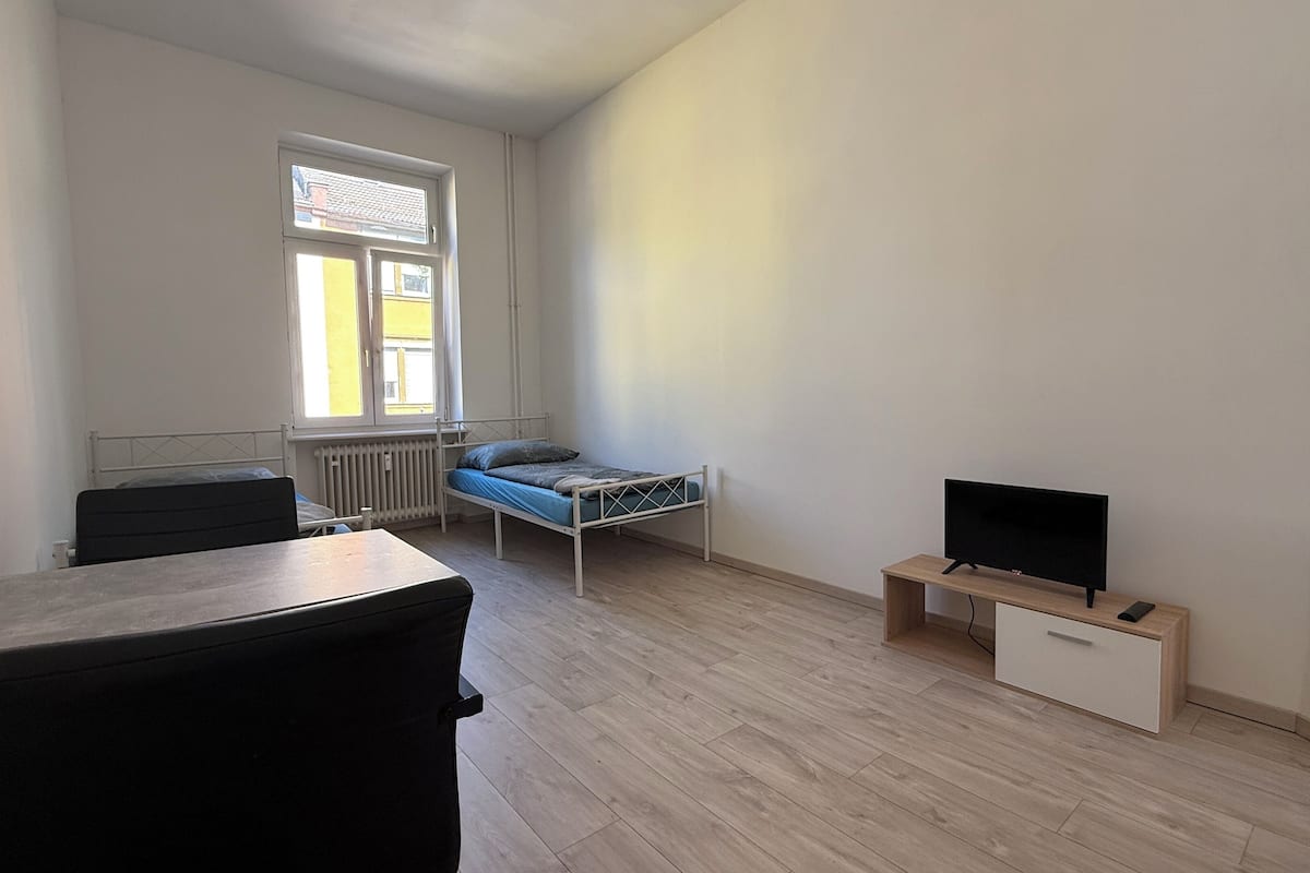 A small, sparsely furnished room with a bed, a desk, and a TV.