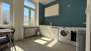 A laundry room with a radiator, washing machines, and a window with a view of buildings.