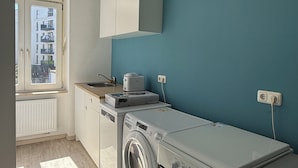 A compact kitchen with a washing machine, oven, and a window with a view of buildings.