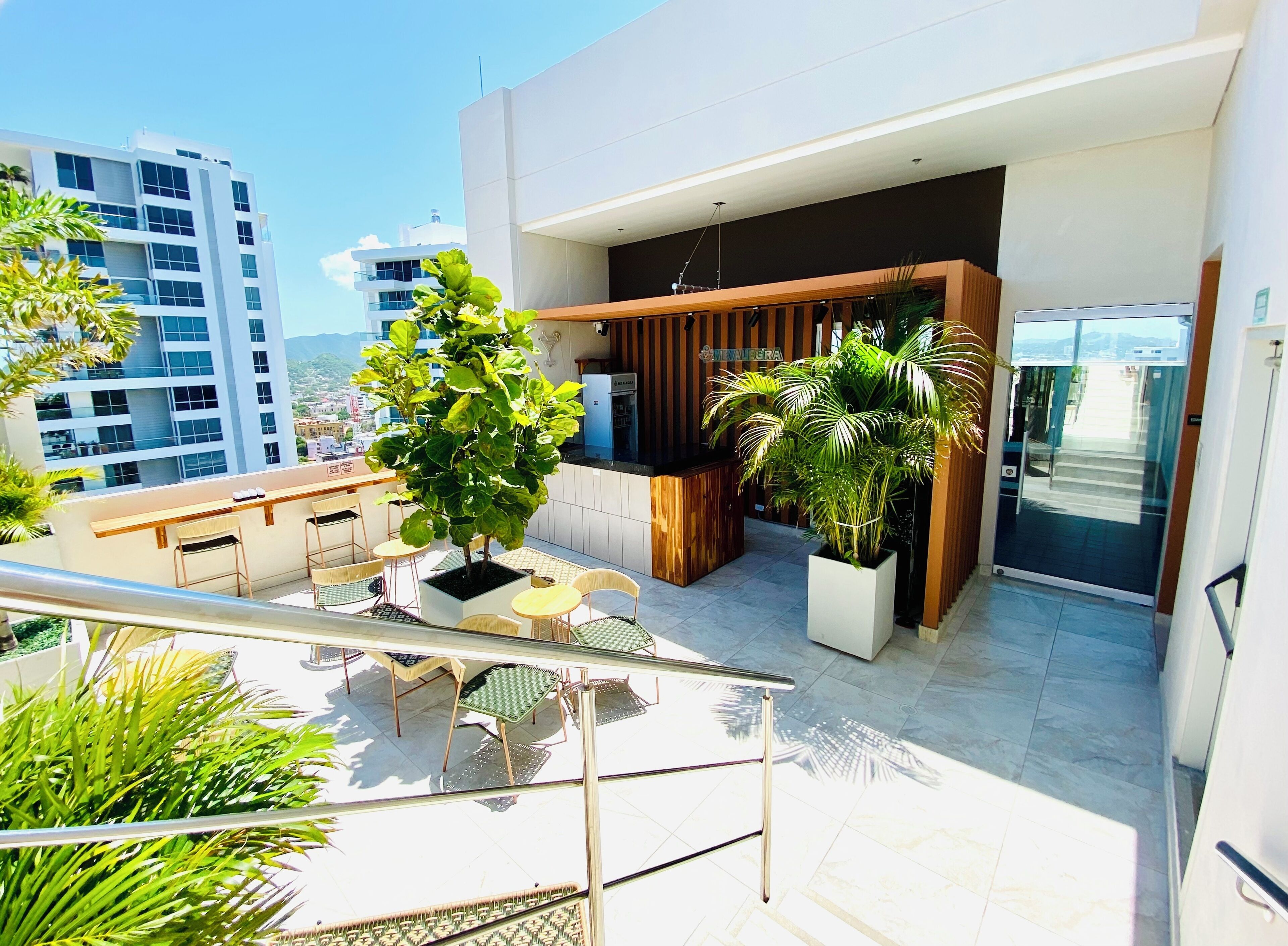 Un balcon extérieur moderne, doté d’un espace salon, de plantes en pot et offrant une vue sur le paysage urbain.