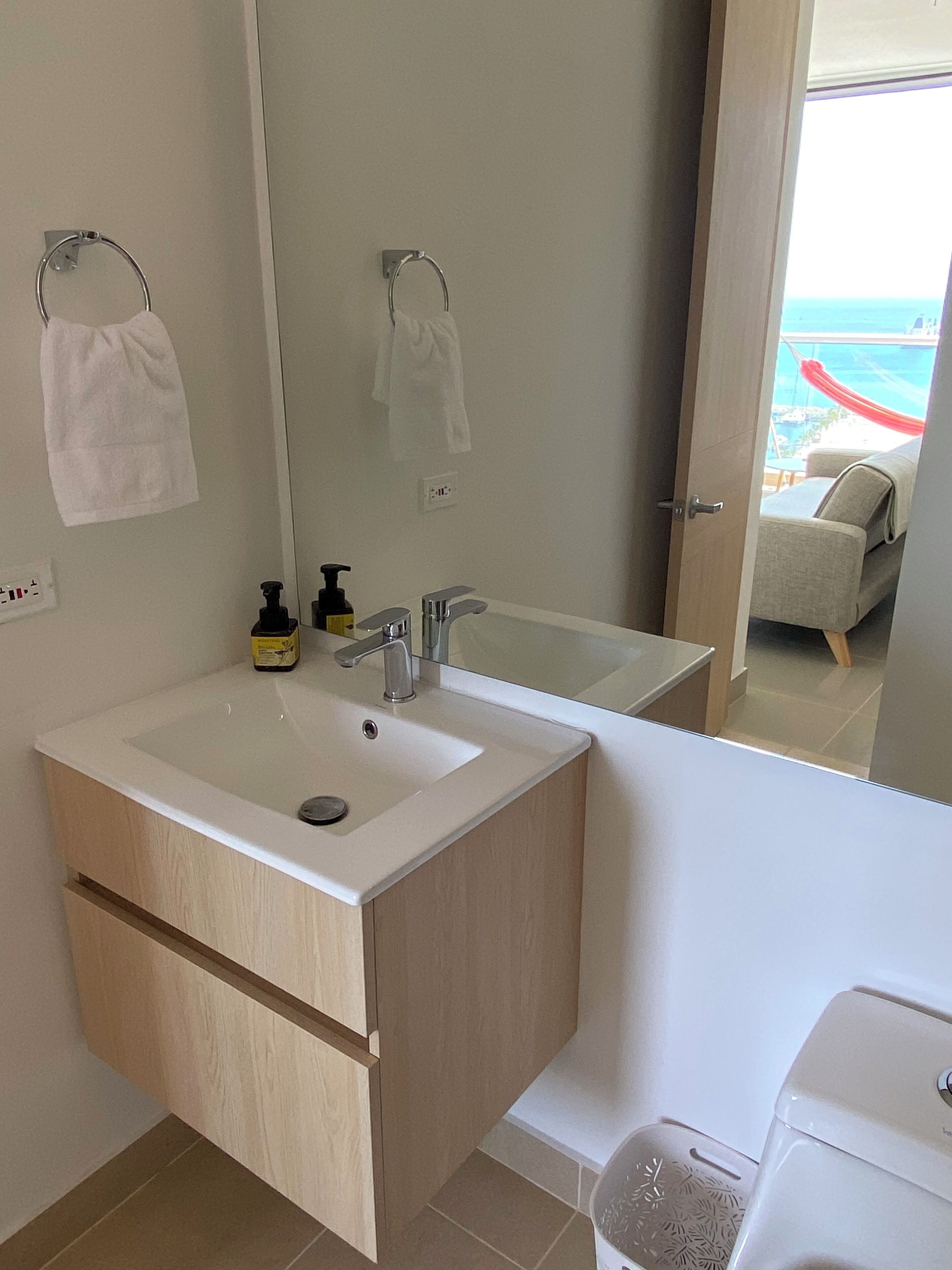 Een moderne badkamer met een groot wastafel, spiegel en uitzicht op een balkon met een rode hangmat.