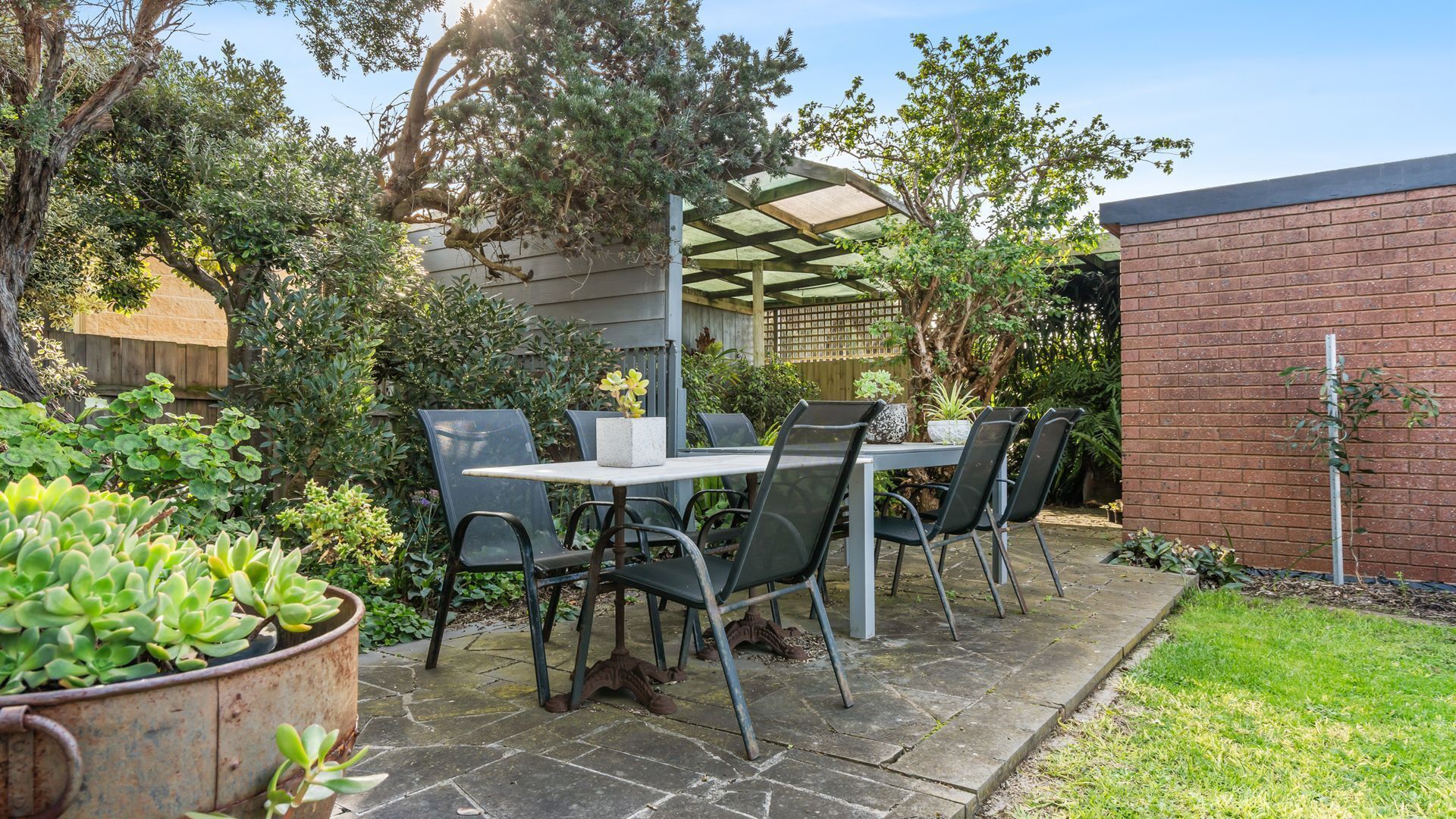 An outdoor patio with a table and chairs, surrounded by greenery and a brick wall.