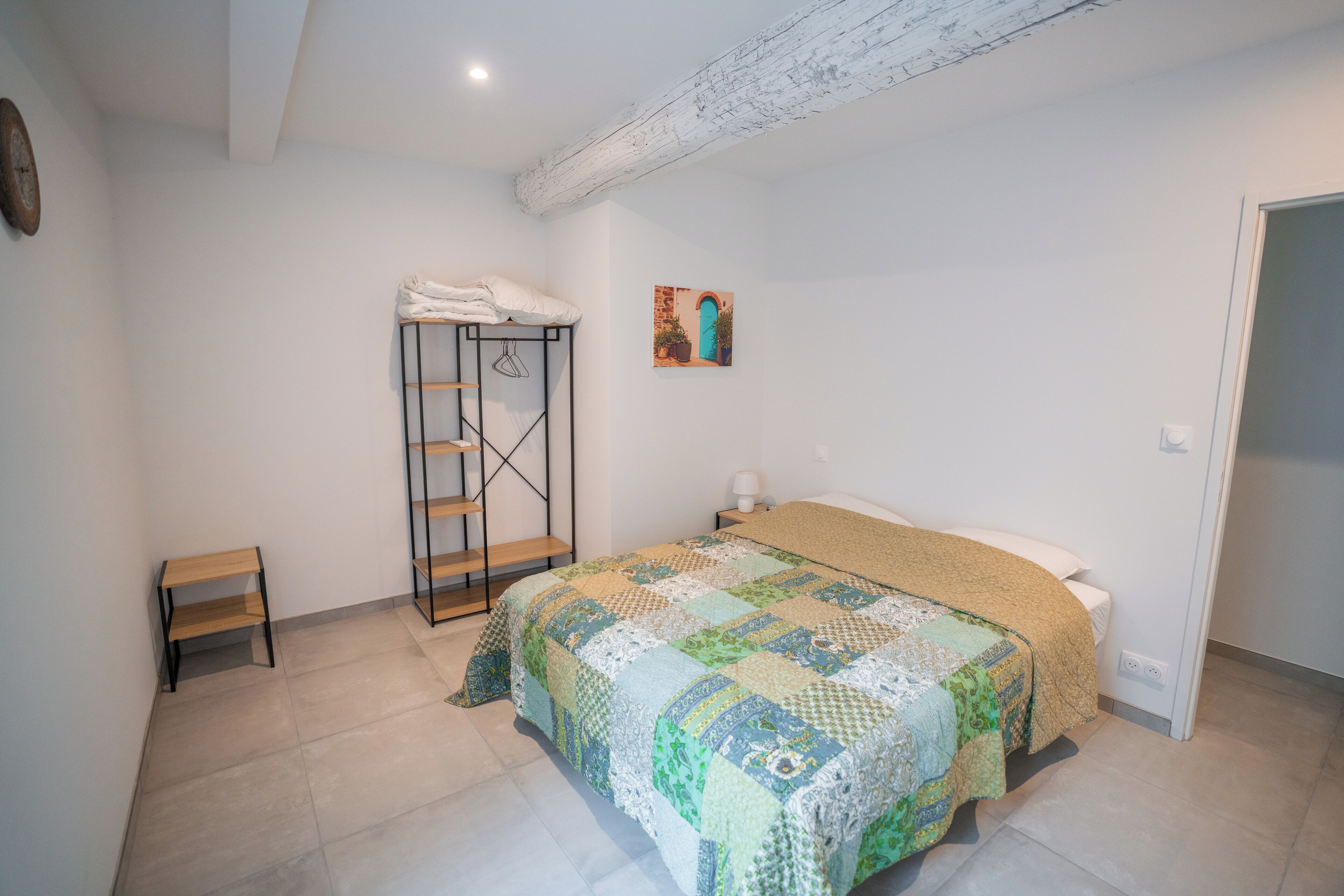A bedroom with a bed, a wardrobe, a small table, and a painting on the wall.