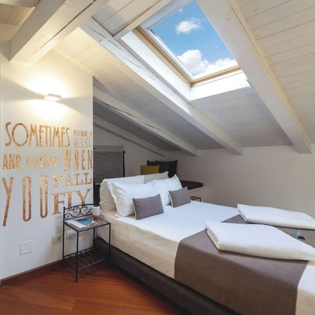 Ein Schlafzimmer mit Oberlicht, einem Bett, einem Nachttisch und einem motivierenden Zitat an der Wand.