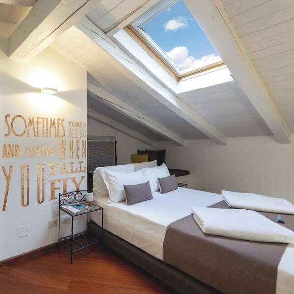 A bedroom with a skylight, a bed, a bedside table, and a motivational quote on the wall.