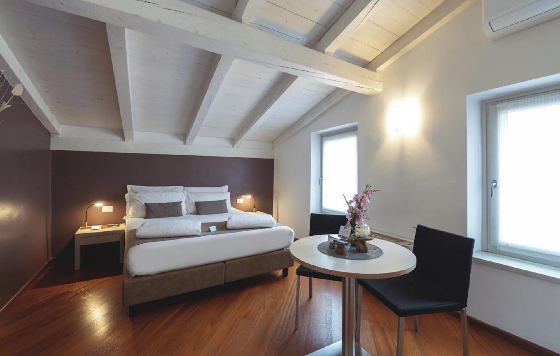 A bedroom with a bed, bedside lamps, a round table with a chair, and a window.